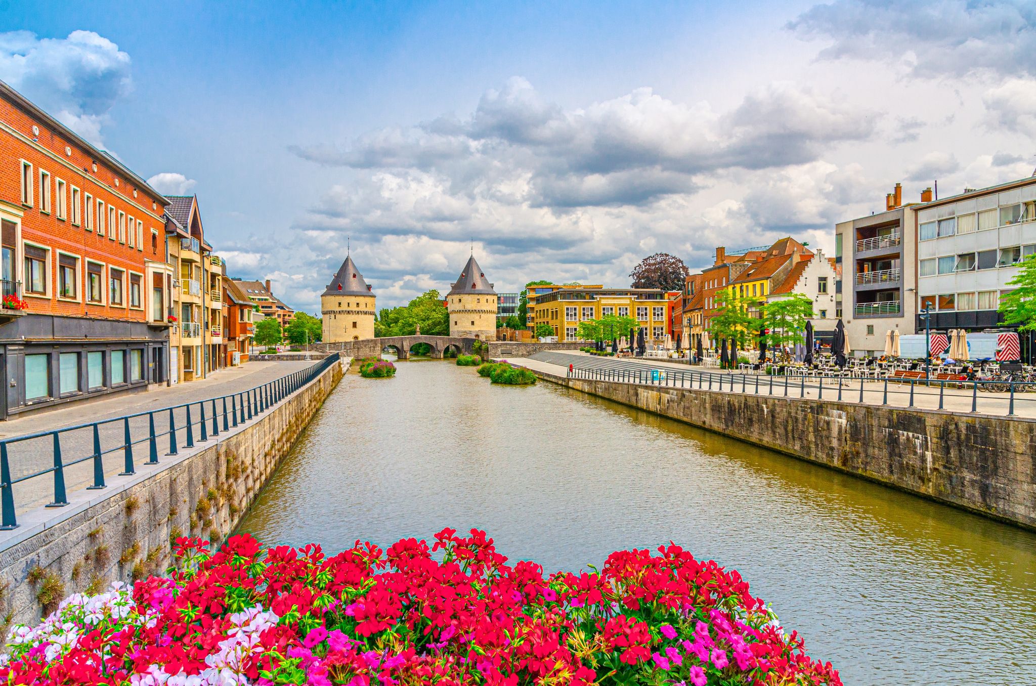photo of view of Kortrijk cityscape, promenade of Lys river, Broel Towers buildings and Broel Bridge in Kortrijk city historical centre, red flowers, belgium landmark, West Flanders province, Flemish Region, Belgium