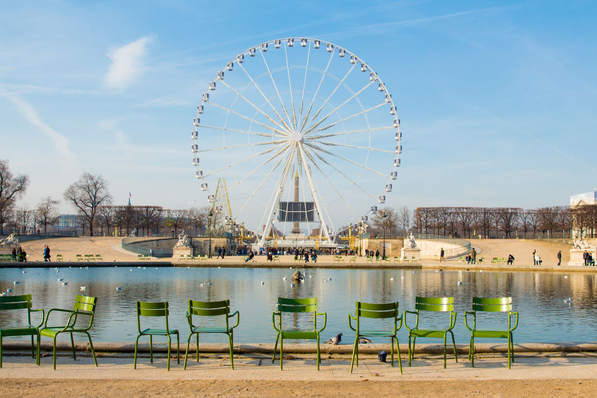 Photo of landscape with a Ferris wheel and empty chairs near pond in the Tuileries garden in Paris, France.