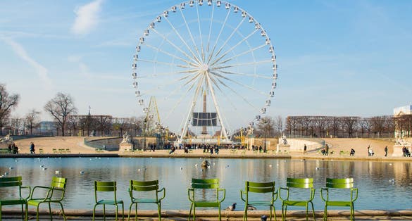 Photo of landscape with a Ferris wheel and empty chairs near pond in the Tuileries garden in Paris, France.