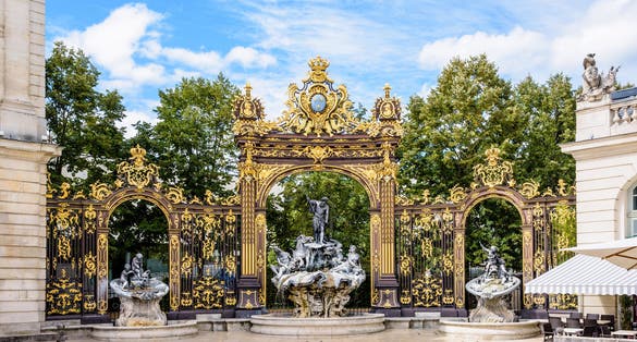 Photo of the fountain of Neptune in the Rococo style and the gilded wrought iron portico in the north-west corner of the Stanislas square in Nancy, France.