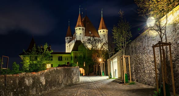 photo of nightscape of Thun, Bernese Oberland, Switzerland. Thun Castle illuminated at night under starry sky.