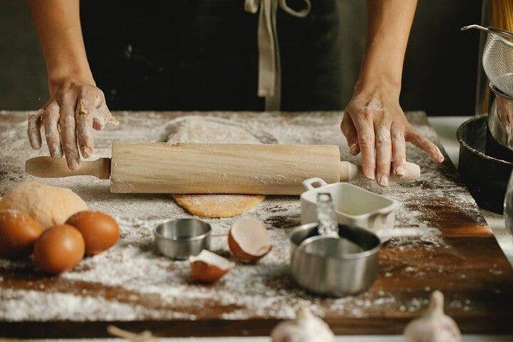 A person rolling dough on a wooden table with flour, eggs, and baking tools in a kitchen in North Macedonia..jpg