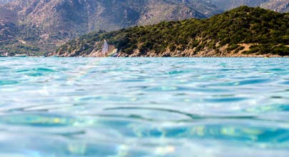 Natural mountainos landscape seen from the blue sea with a windsurf behind. Villasimius (Sardinia), Campulongu beach.