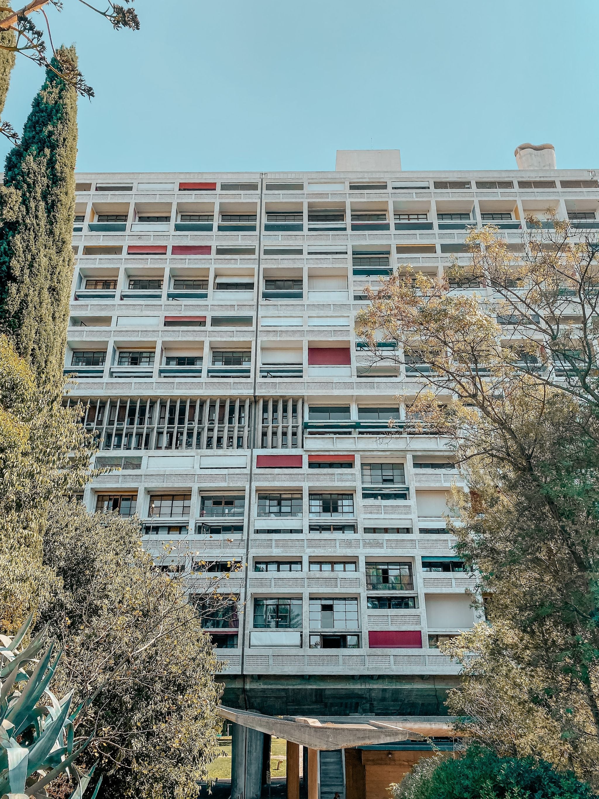 Cité Radieuse in Marseille, a modernist apartment building by Le Corbusier with a grid-like facade and colorful panels, seen through trees on a sunny day..jpg