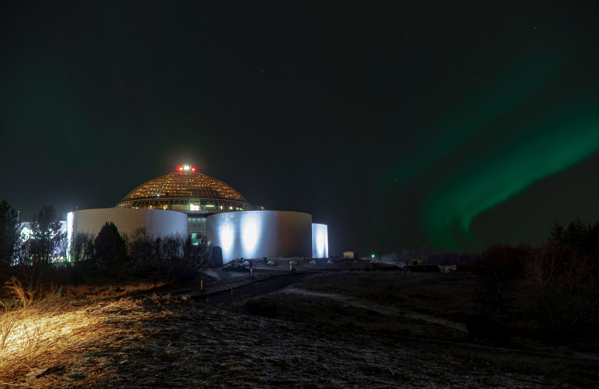 photo of the green northern lights over the illuminated perlan museum in Reykjavik, Iceland.