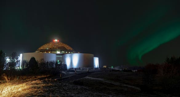 photo of the green northern lights over the illuminated perlan museum in Reykjavik, Iceland.