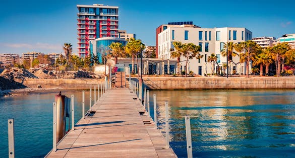 Stunning spring cityscape of Vlore port with old wooden pier. Calm morning seascape of Adriatic sea. Bright outdoor scene of Albania, Europe. Traveling concept background.