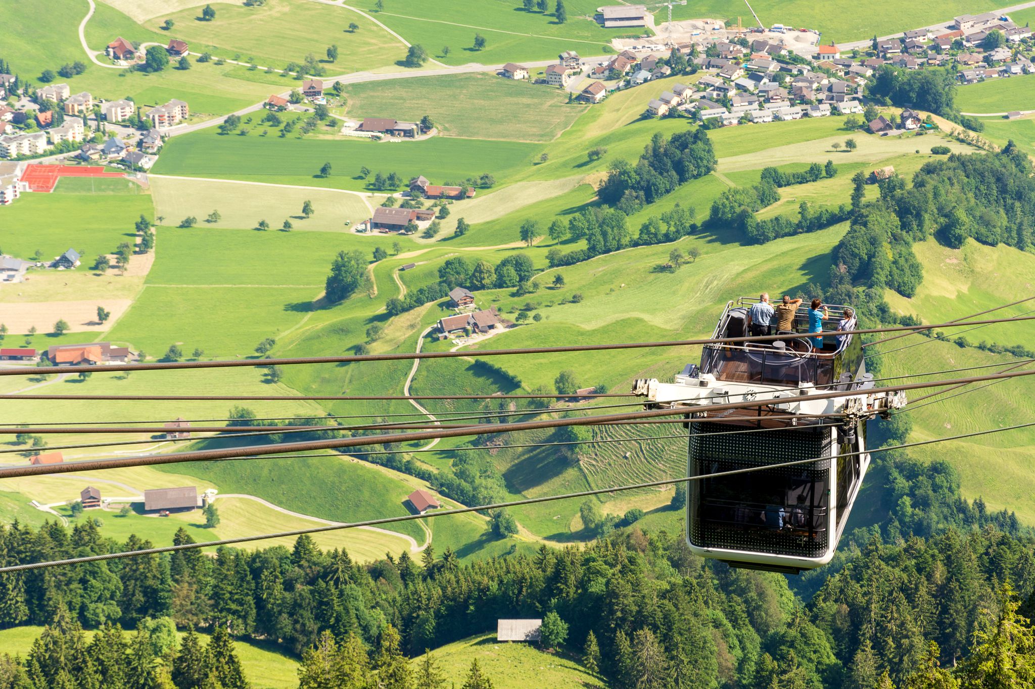 photo of tourists (faces not visible) climbing the cable car in an open car up Mount Stanserhorn in Switzerland and admire the magnificent aerial panorama of central Switzerland, mountains, villages and forest.