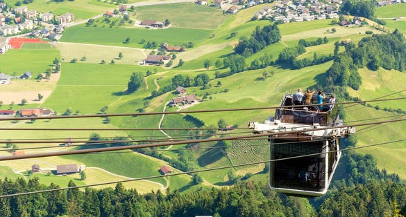 photo of tourists (faces not visible) climbing the cable car in an open car up Mount Stanserhorn in Switzerland and admire the magnificent aerial panorama of central Switzerland, mountains, villages and forest.