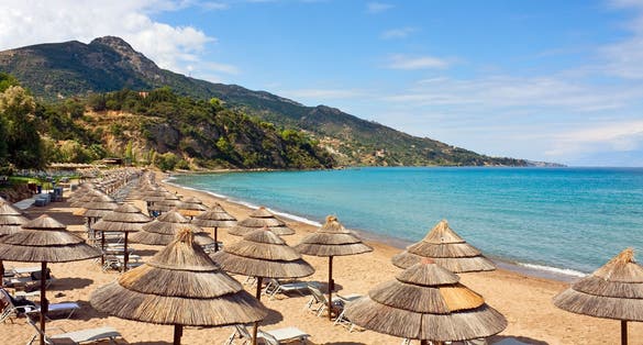 Photo of row of Straw umbrellas and lounges at sandy beach Zakynthos, Greece.