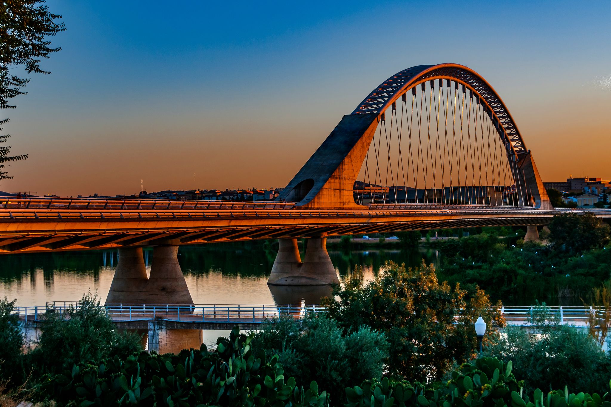 Photo of Sunset at Lusitania bridge. It has an arch of 190 meters of steel from which hang 23 pairs of pendulums with both ends in concrete. 