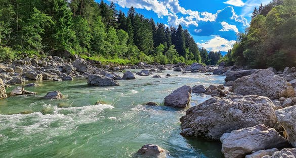 River Gail flowing through the Schuett in the natural park Dobratsch in Villach, Carinthia, Austria. Gailtaler and Villacher Alps. Riverbank is full of massive rocks. Swimming in crystal clear water