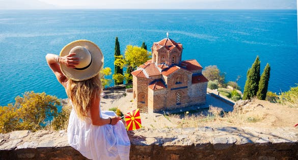 Photo of woman in white dress and Macedonian flag enjoying Ohrid lake, North Macedonia.