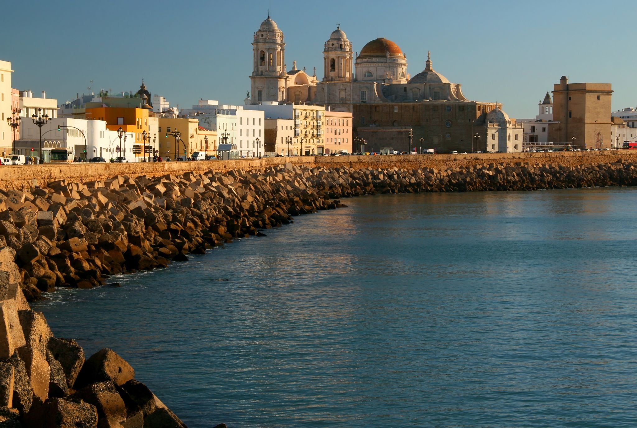 photo of the promenade in the city of Cadiz (Andalusia region, southern Spain) with the blue waters of the Atlantic Ocean and the Catedral de Cadiz building in the background.