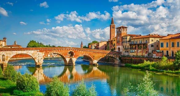 Panoramic view to Bridge Ponte Pietra in Verona on Adige river. Veneto region. Italy. Sunny summer day panorama and blue dramatic sky with clouds. Ancient european italian terracotta color houses