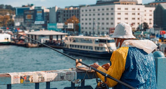  Elder man wearing colorful raincoat fishing at Galata Bridge in Golden Horn, Istanbul. Rod fishing from Galata Bridge very popular.