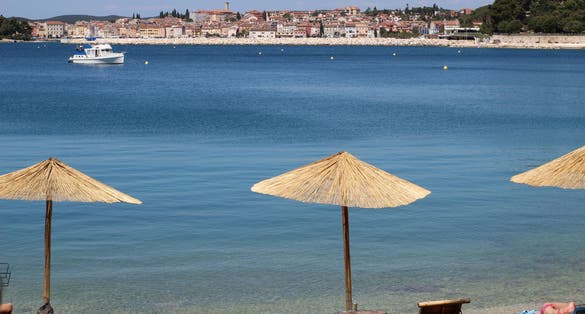 Photo of sunshades and sunbeds on a Golden Cape park beach with a view of Rovinj, Croatia.
