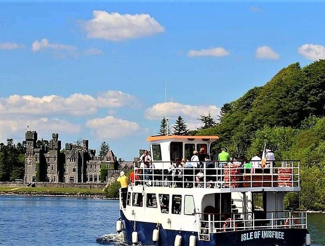 A tour boat named Isle of Innisfree cruises on Lough Corrib, Ireland, with a historic castle and green trees in the background..jpg