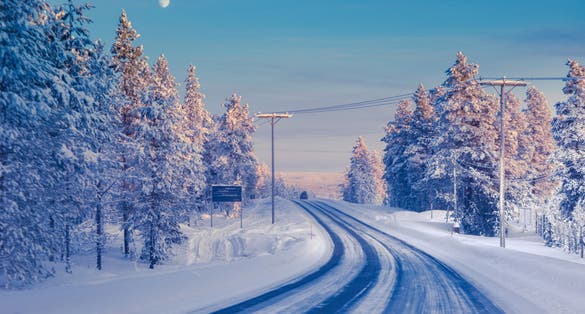 Photo of winter landscape with snow-covered road and pine trees, Ivalo.