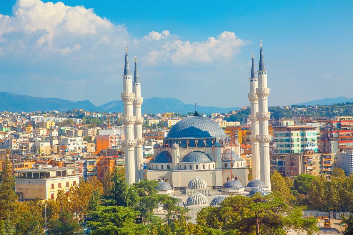 A beautiful mosque with four tall minarets stands in the middle of a colorful city with mountains in the background..jpg