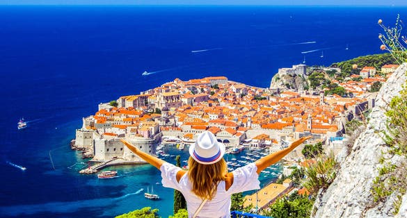 Photo of happy woman enjoys beautiful landscape view of old town (medieval Ragusa) and Dalmatian Coast of Adriatic Sea in Dubrovnik, Croatia.