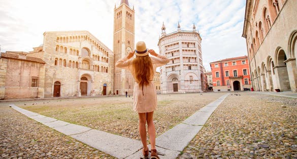 photo of view of Young female tourist standing back on the central square with cathedral and famous leaning tower on the background in Parma town. Having great vacations in Parma, Italy.
