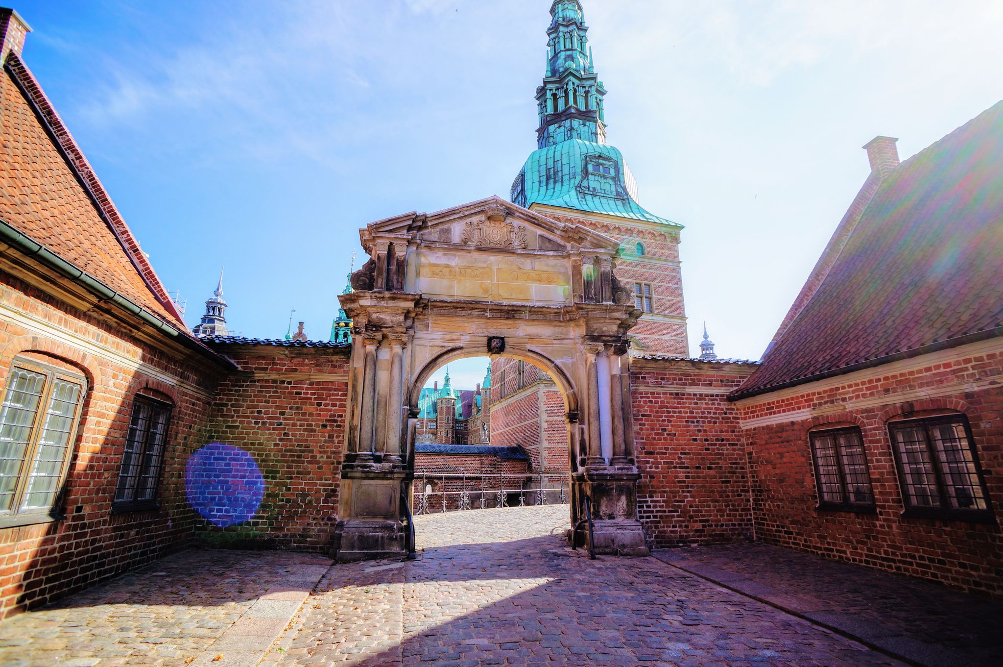 Photo of entrance to Frederiksborg palace. Red brick fortress wall, archway and green copper spiels of towers of renaissance castle Frederiksborg, Denmark.