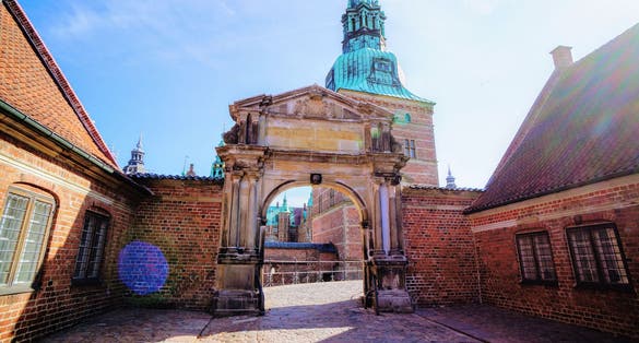 Photo of entrance to Frederiksborg palace. Red brick fortress wall, archway and green copper spiels of towers of renaissance castle Frederiksborg, Denmark.