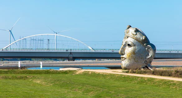 Huge replica of a Roman mask on the banks of the Waal with the Lentloper Bridge in the background. It is called the face of Nijmegen. Oosterhoutsedijk Gelderland, Netherlands