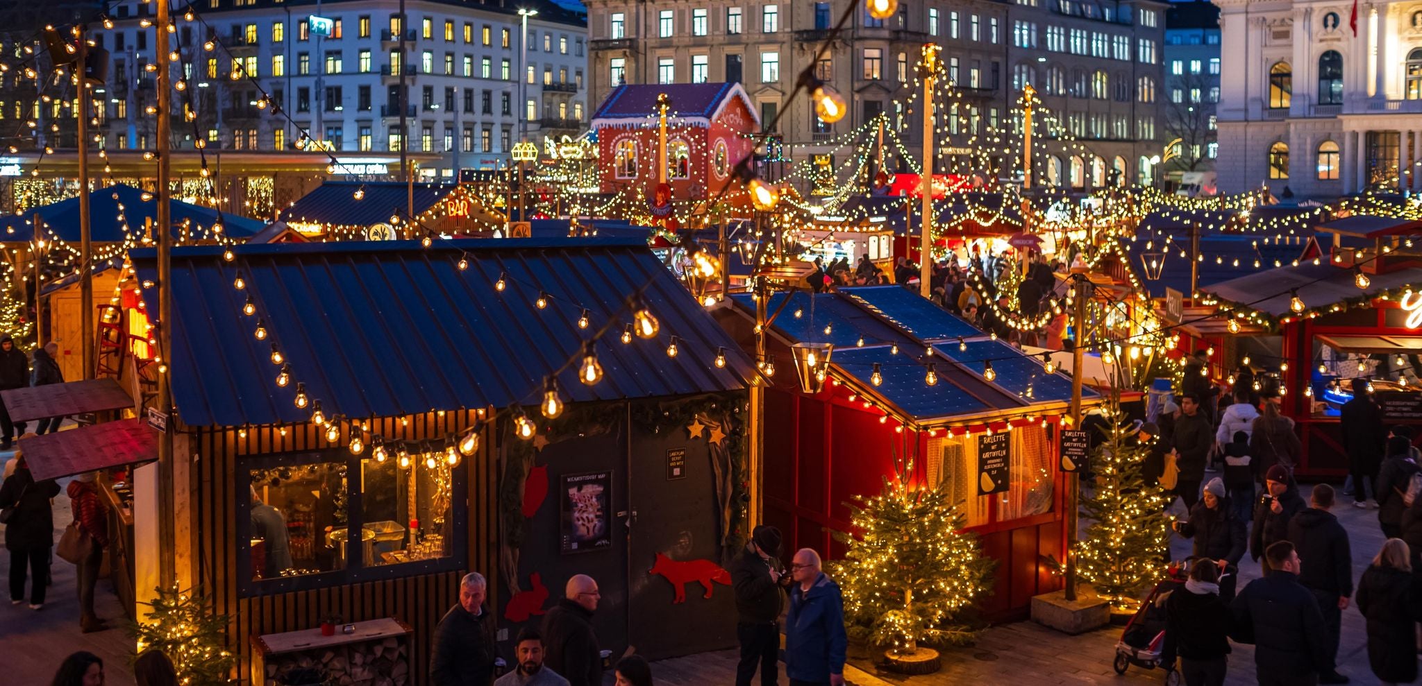 Zurich Christmas Market at night with festive lights, decorated stalls, and crowds in front of the Opera House..jpg