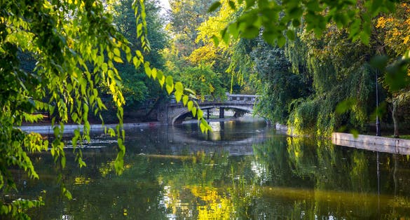 Photo of old stone bridge over the quiet lake with beautiful autumn light in the park. Cismigiu Garden, Bucharest, Romania.