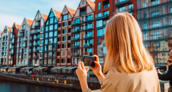 Photo of view of lady tourist takes photo or video on smartphone at city of Gdansk, Poland.