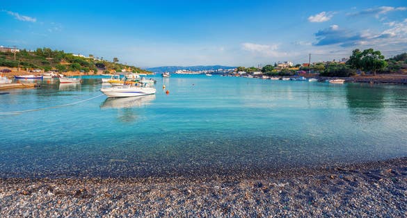 Photo of beach and small natural harbor with anchored fishing boats with the beautiful town of Agios Nikolaos at the background, Crete, Greece.