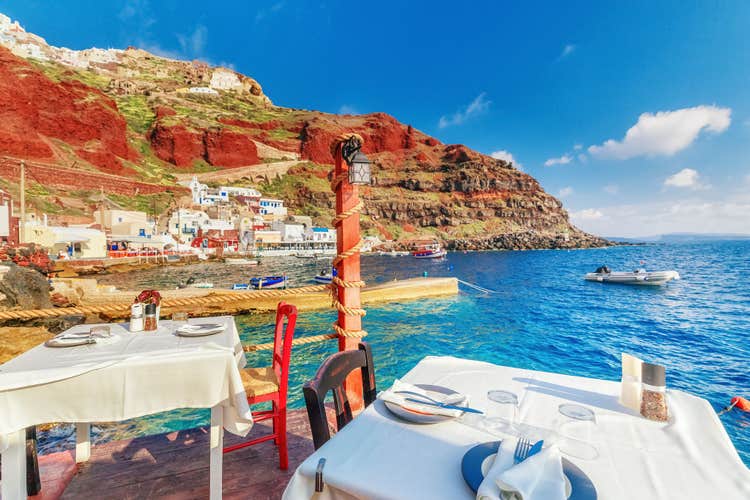 Greece, Santorini. Restaurant with served table in seafront of Aegean sea on Santorini Cyclades island with breathtaking, amazing and unbelievable view on the water and embankment of Oia Ia village.
