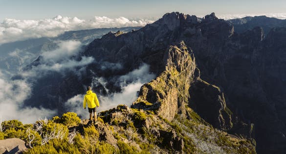 Man stands alone on the peak of rock. Beautiful moment the miracle of nature. Colorful mist in valley. Man hike. Trekking from Pico do Arieiro to Pico Ruivo, Madeira island, Portugal.
