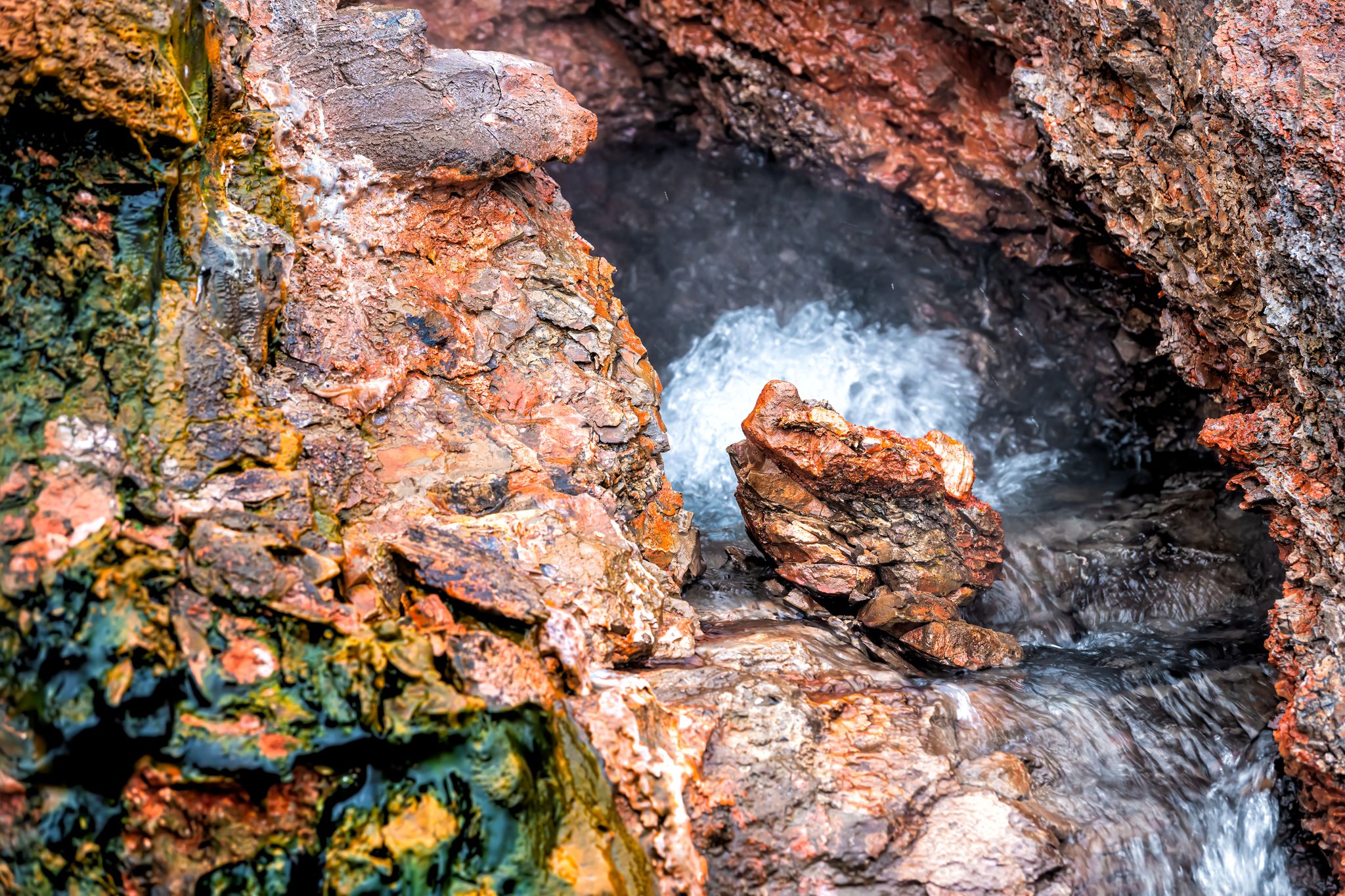 Closeup of steam geyser in Deildartunguhver hot springs in Iceland with red rock colorful cave opening hole and water boiling .
