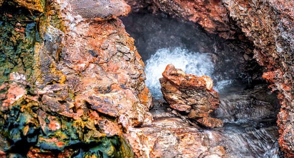 Closeup of steam geyser in Deildartunguhver hot springs in Iceland with red rock colorful cave opening hole and water boiling .