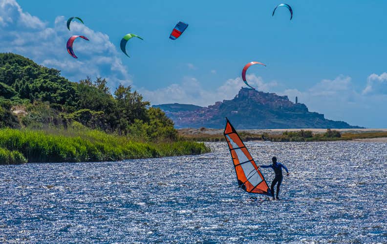 Windsurfers and kitesurfers on the beaches of Valledoria with the old village of Castesardo in the background, Sardinia, Italy