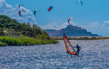 Windsurfers and kitesurfers on the beaches of Valledoria with the old village of Castesardo in the background, Sardinia, Italy