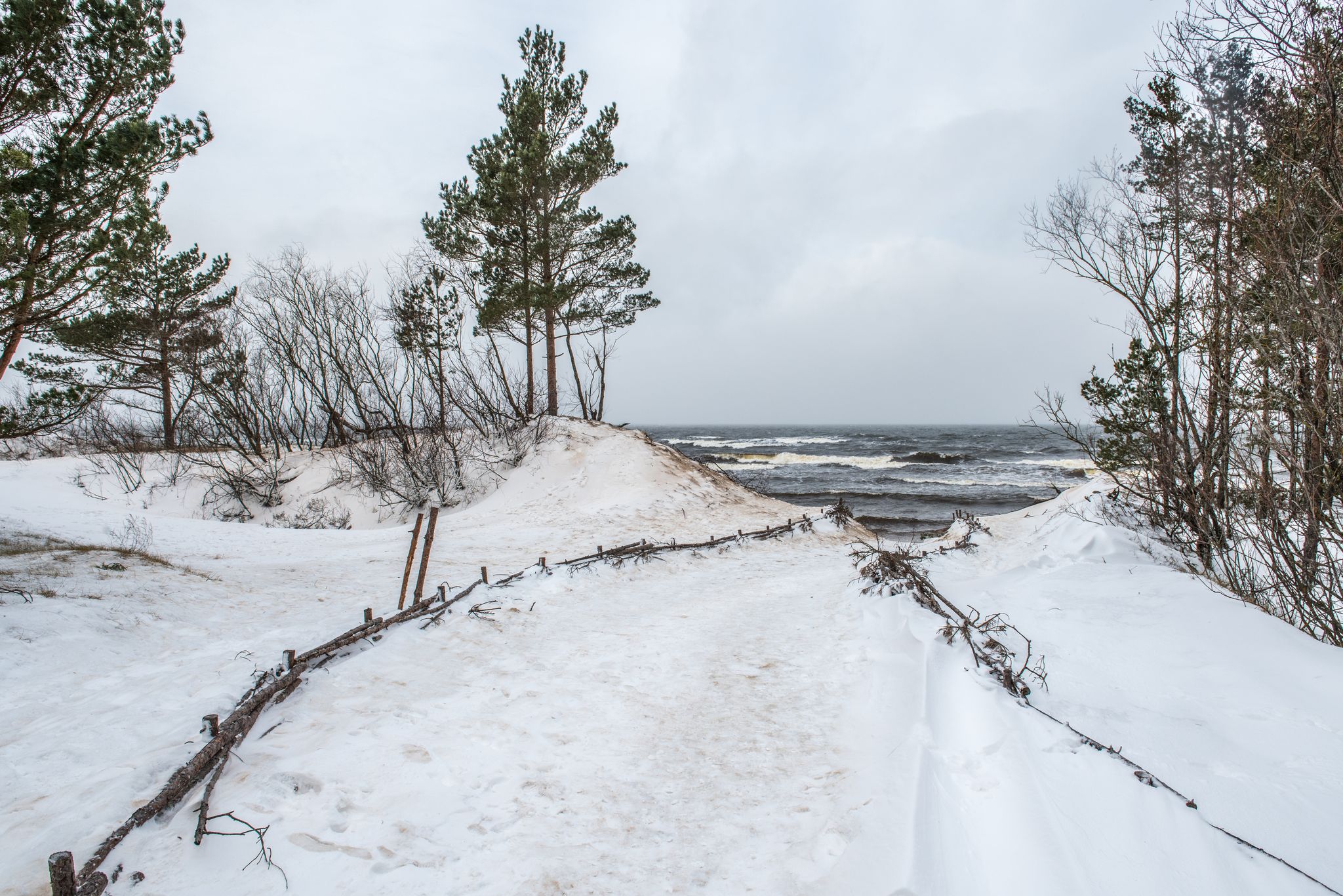 photo of Baltic sea beach is snowy in winter and there are big waves in the sea. Footpath between winter Baltic sea s dunes in Saulkrasti in Latvia.