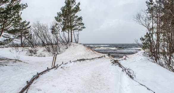 photo of Baltic sea beach is snowy in winter and there are big waves in the sea. Footpath between winter Baltic sea s dunes in Saulkrasti in Latvia.