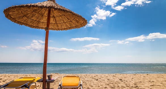 Photo of straw umbrella with deck chairs on a sandy beach by the sea. The Paralia, a tourist seaside part of the municipality Katerini, Greece.