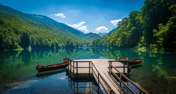 Photo of panoramic view of Biogradsko lake. Virgin forests and beautiful mountains, wooden pier and boats.