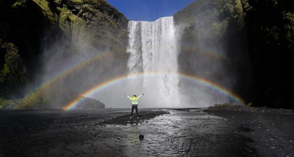 photo of tourist looking at the famous skógafoss waterfall in Iceland.