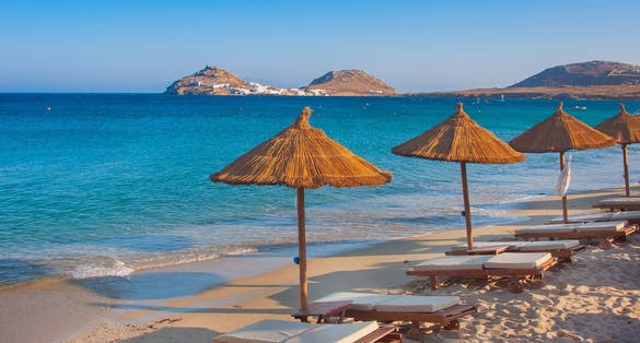 Photo of the sandy beach near the blue sea with sun beds and umbrellas, Mykonos, Greece.