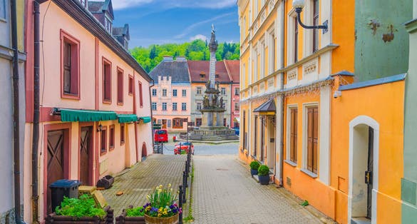 Photo of Narrow street of Loket town with colorful traditional typical buildings, street flowers and Column of the Holy Trinity at Marketplace square, Karlovy Vary Region, West Bohemia, Czech Republic.