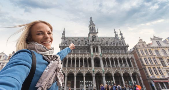 Photo of a woman in casual clothes takes selfie pictures on her phone in the background of the Brussels City Museum in the main square Grand place, Belgium .