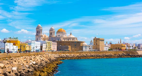 photo of beautiful view at day of the cathedral of Cadiz called cathedral de Santa Cruz with its 2 towers and its golden dome a blue sky and a blue ocean in Cadiz Andalusia Spain Europe.