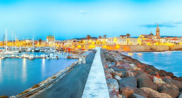 Panoramic evening cityscape of Alghero port and historical part of city.