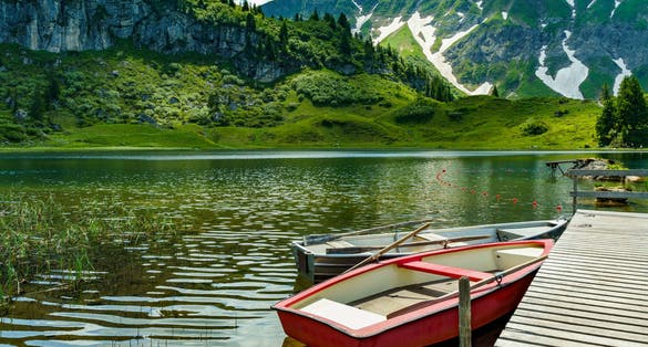 Rowing boats on the Körber lake in the mountains of the Bregenz Forest. anytime changing weather with sun and clouds illuminate the flowered meadows from three stage alpine farming around the lake